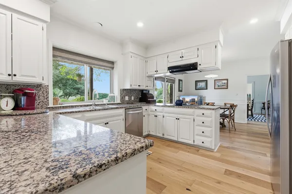 a kitchen with stainless steel appliances granite countertop a stove a sink a refrigerator and white cabinets with wooden floor