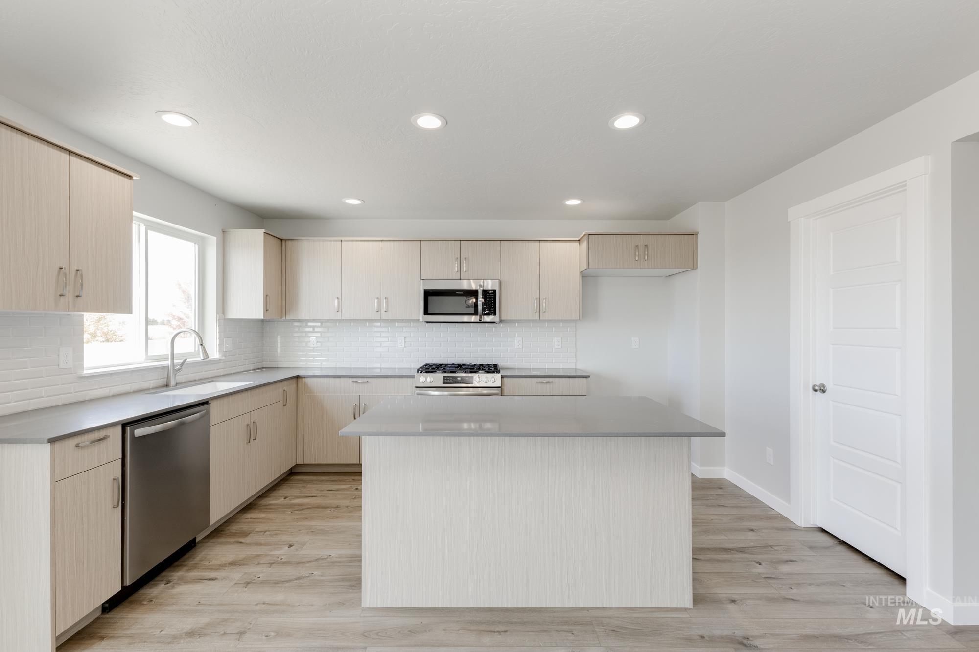 12853 Decatur Street Nampa, ID 83651 - Photo 4 of 24 Modern kitchen featuring light wood-finish cabinetry, stainless steel appliances, a center island with countertop, a white subway tile backsplash, and wood-finish flooring