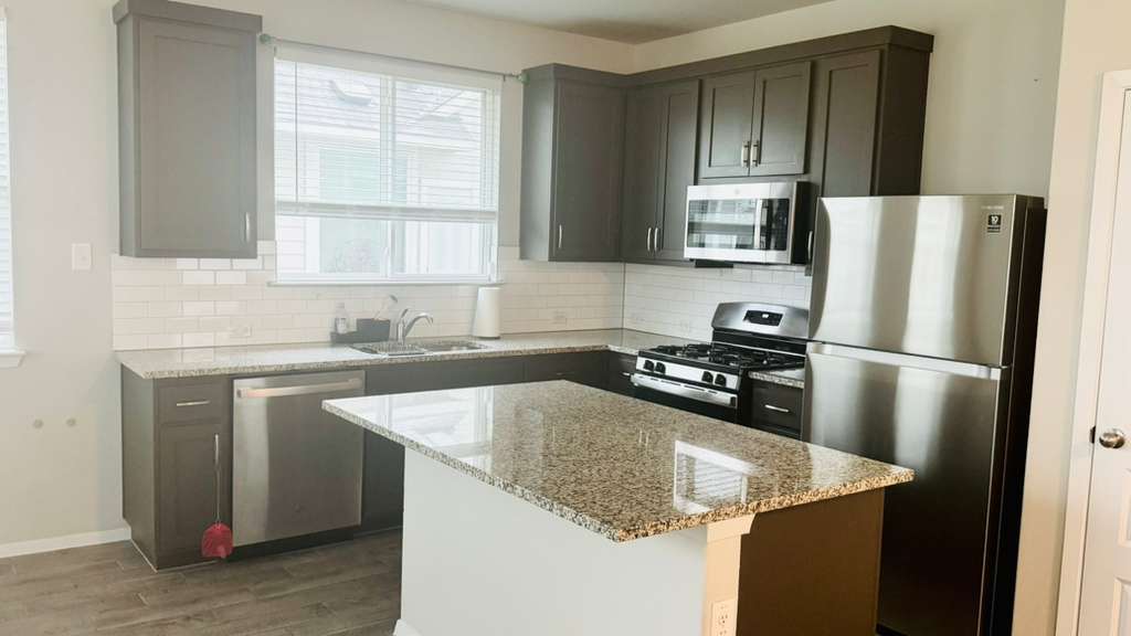 1305 Goforth Road Kyle, TX 78640 - Photo 10 of 23 Kitchen featuring stainless steel appliances, light stone countertops, and dark wood finish cabinets