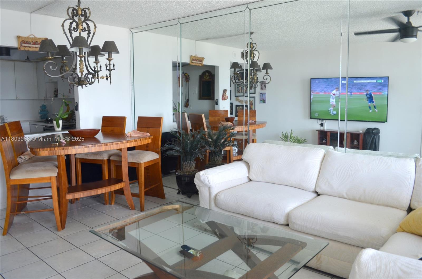 13499 Biscayne Boulevard, Unit 702 North Miami, FL 33181 - Photo 10 of 31 a living room with furniture a chandelier and a flat screen tv