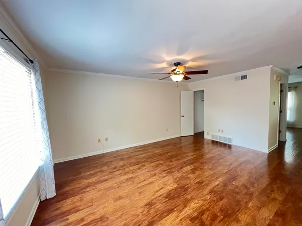 an empty room with wooden floor fan and windows