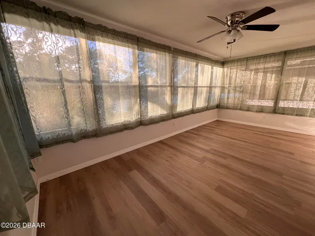 an empty room with wooden floor chandelier fan and windows