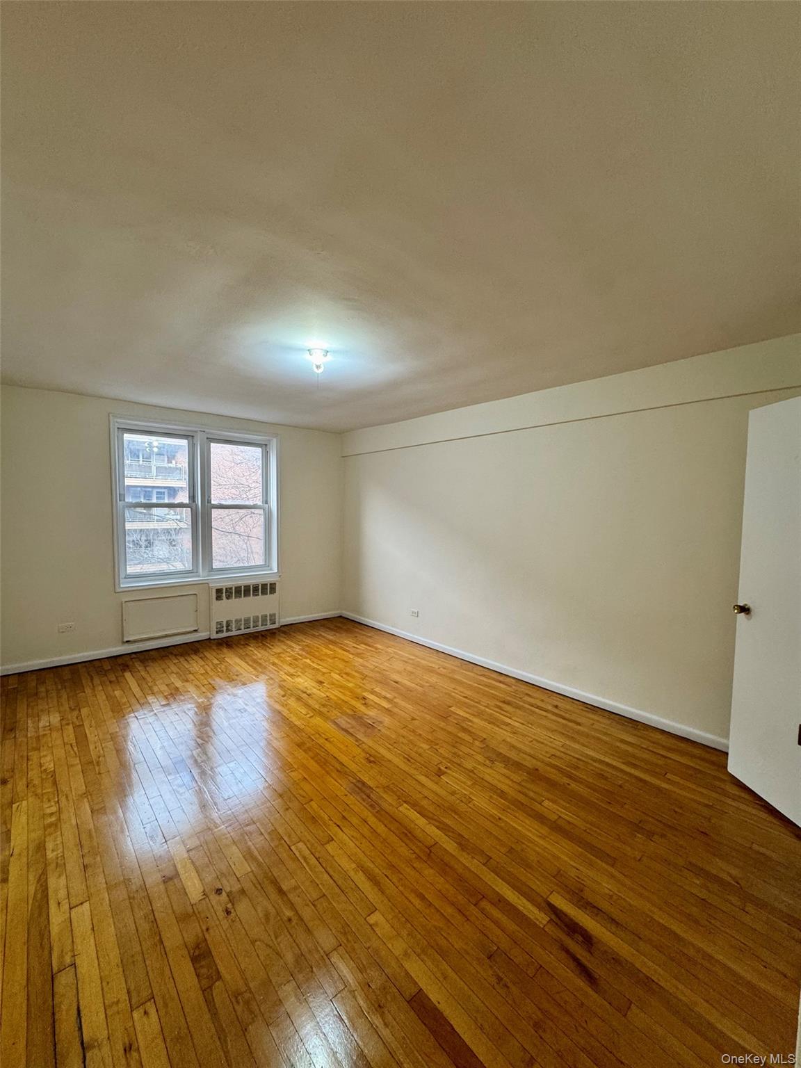 142-20 41st Avenue, Unit 4K Queens, NY 11355 - Photo 3 of 8 Spare room featuring light wood-type flooring and radiator heating unit