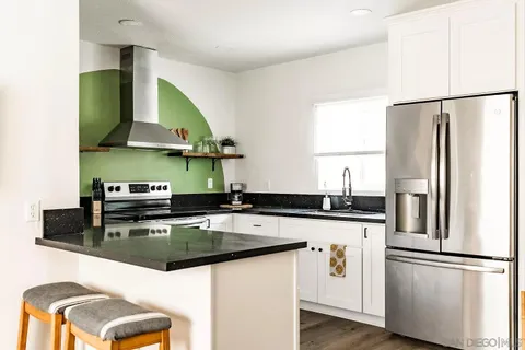 a living room with stainless steel appliances wooden floor and a flat screen tv