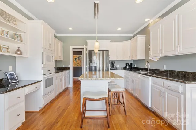 a large kitchen with granite countertop lots of white cabinets stainless steel appliances a dining table and chairs