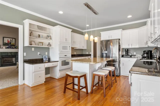 a kitchen with stainless steel appliances granite countertop a stove a refrigerator a kitchen island a stove a dining table and chairs with wooden floor