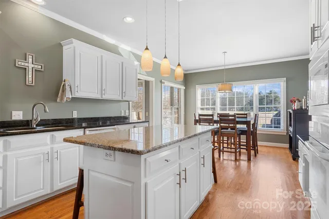 a kitchen with stainless steel appliances granite countertop a stove top oven a sink a dining table and chairs with wooden floor