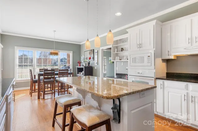 a kitchen with granite countertop a table chairs stove and white cabinets