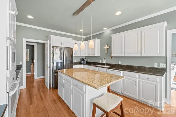 a kitchen with stainless steel appliances granite countertop a refrigerator a sink dishwasher a stove and white countertops with wooden floor