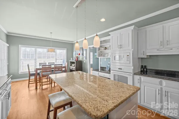 a kitchen with granite countertop a stove a sink a dining table and chairs with wooden floor