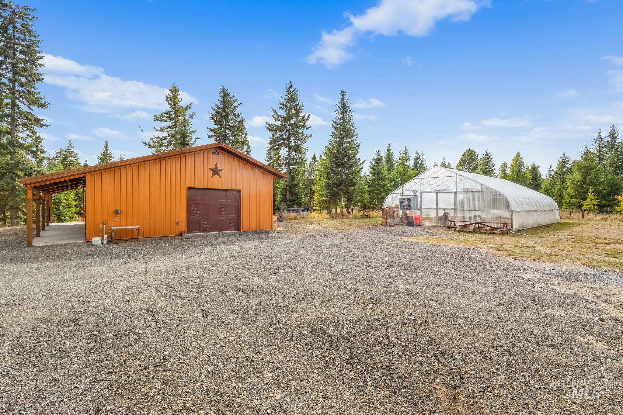 3989 East Mountain Road Anatone, WA 99401 - Photo 33 of 49 Metal-sided outbuilding with attached covered parking, gravel drive, and a large clear-span greenhouse structure
