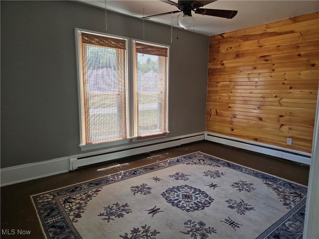 5555 Detroit Road Sheffield, OH 44054 - Photo 4 of 50 Unfurnished room featuring wood walls, ceiling fan, a baseboard radiator, and a baseboard heating unit