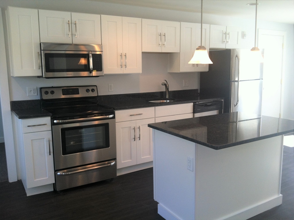 a kitchen with granite countertop a stove and a microwave with cabinets