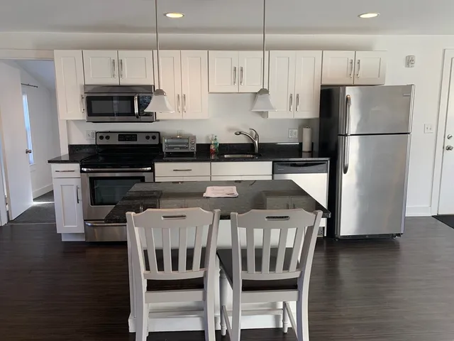 a kitchen with stainless steel appliances granite countertop a refrigerator a stove a microwave oven a sink a dining table and chairs with wooden floor