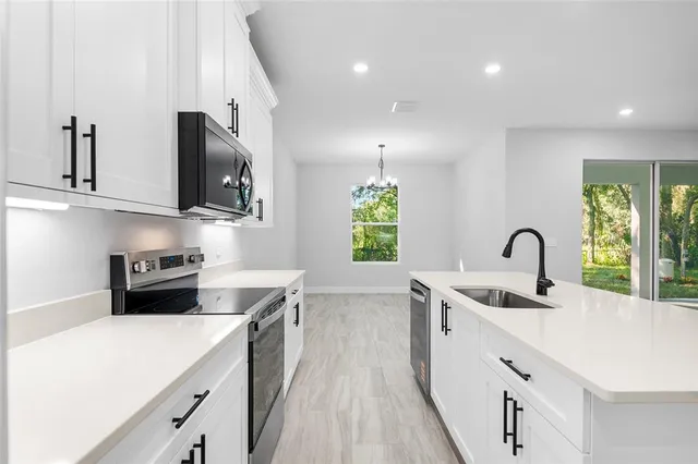 a kitchen with stainless steel appliances a sink stove and white cabinets with wooden floor
