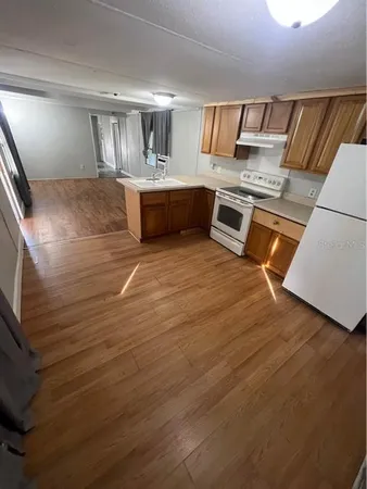 a view of kitchen and empty room with wooden floor