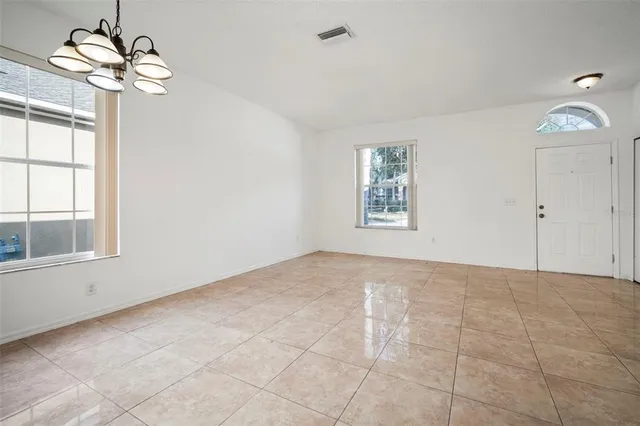 an empty room with chandelier fan and windows