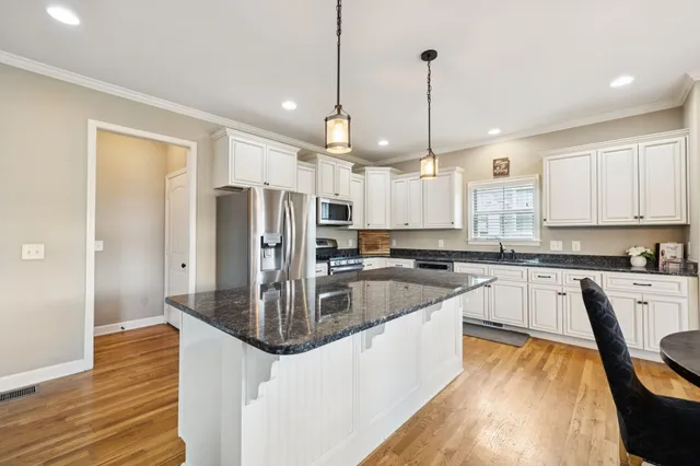 a kitchen with stainless steel appliances kitchen island granite countertop a refrigerator a sink dishwasher a stove and white countertops with wooden floor