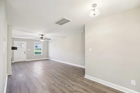 an empty room with wooden floor chandelier fan and windows