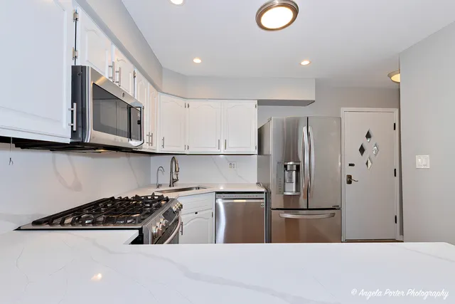 a kitchen with stainless steel appliances granite countertop a sink a stove a refrigerator a microwave oven with white cabinets