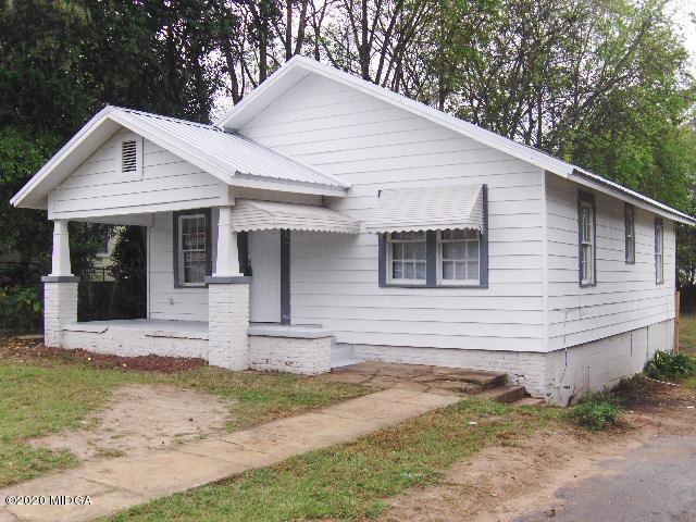 a view of a white house with a small yard plants and large tree