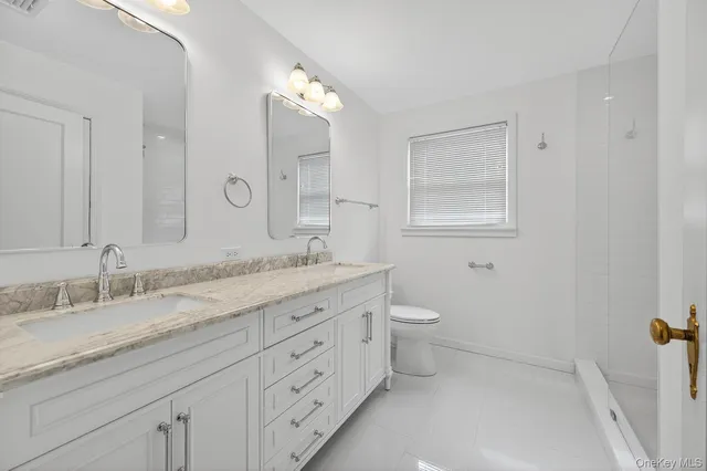 a bathroom with a granite countertop double vanity sink a mirror and a toilet