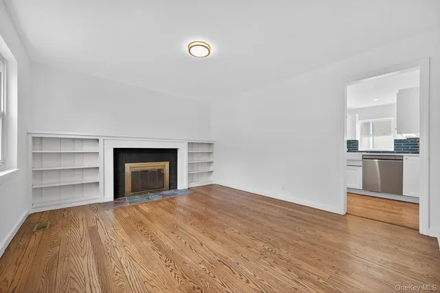 a view of empty room with wooden floor and kitchen