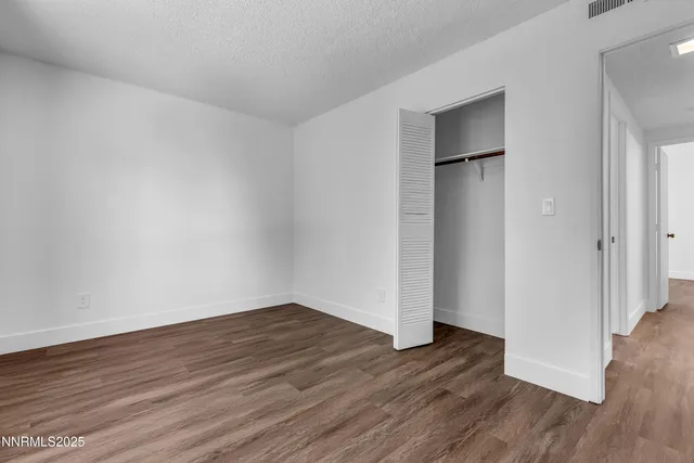 a view of an empty room with wooden floor and closet