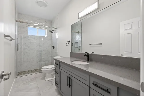 a bathroom with a granite countertop sink a toilet a mirror and shower