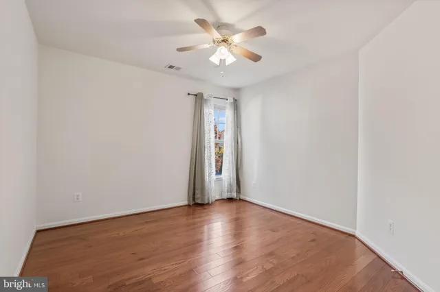 a view of an empty room with wooden floor and a ceiling fan