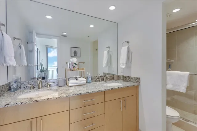 a bathroom with a granite countertop double vanity sink mirror and toilet