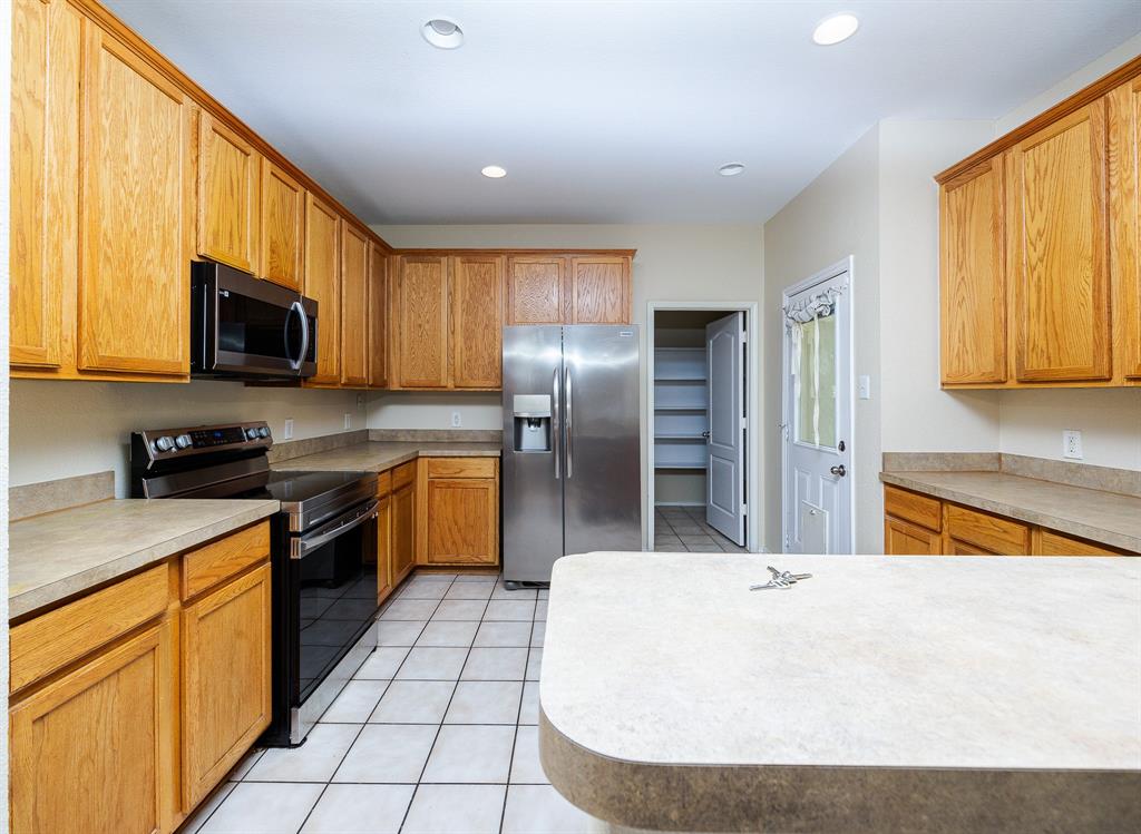 1828 Mercer Way Savannah, TX 76227 - Photo 14 of 38 Kitchen with stainless steel appliances, light tile patterned floors, light countertops, recessed lighting, and brown cabinetry