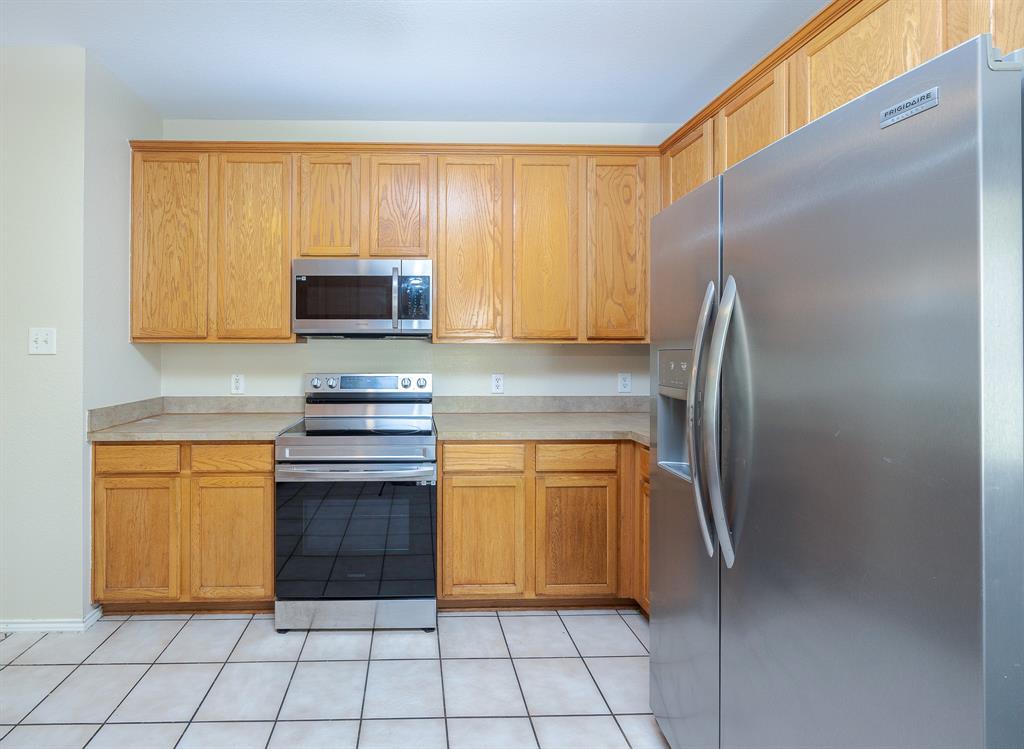 1828 Mercer Way Savannah, TX 76227 - Photo 16 of 38 Kitchen featuring stainless steel appliances, light countertops, light tile patterned flooring, and brown cabinets