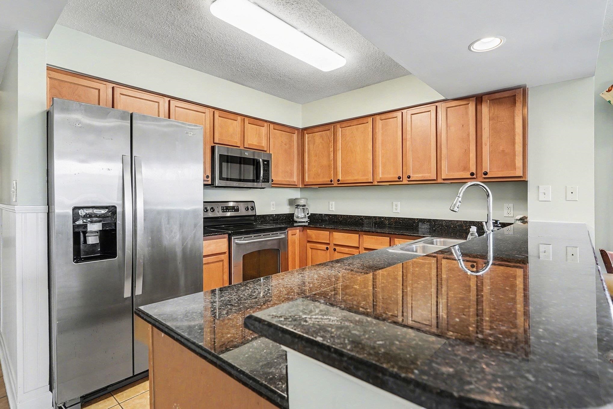 1707 Perrin Drive, Unit 701 North Myrtle Beach, SC 29582 - Photo 11 of 40 Kitchen with appliances with stainless steel finishes, dark stone counters, brown cabinetry, a peninsula, and a textured ceiling