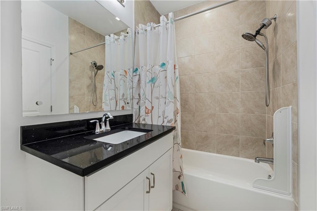 7549 Carnegie Way Naples, FL 34119 - Photo 11 of 22 a bathroom with a granite countertop sink a mirror a bathtub and a shower