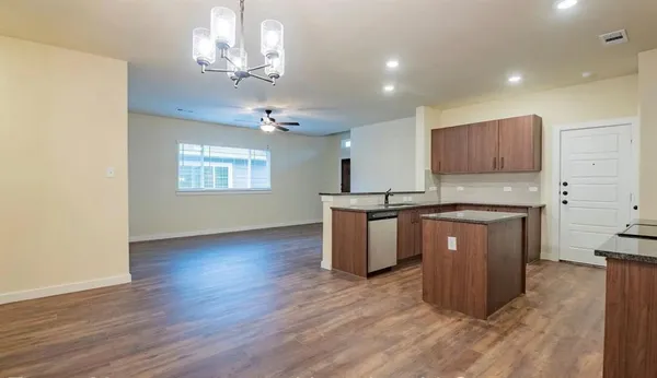 a kitchen with kitchen island granite countertop a stove top oven a sink cabinets and wooden floor