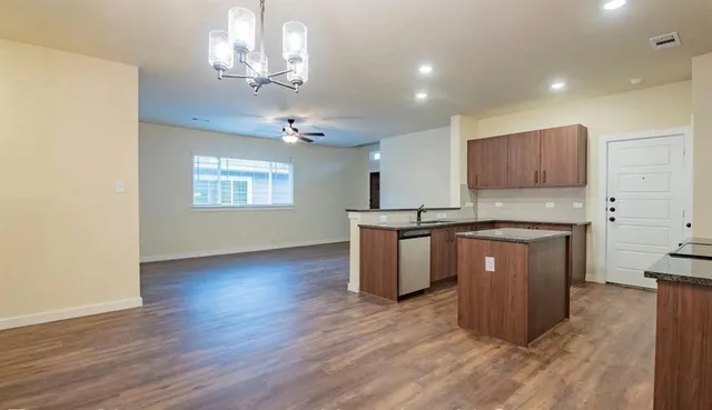 a kitchen with kitchen island granite countertop a stove top oven a sink cabinets and wooden floor