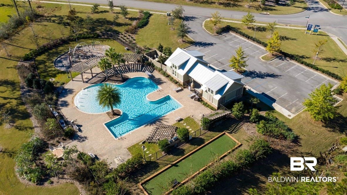 32125 Lyon Road Daphne, AL 36527 - Photo 62 of 70 Community amenity center featuring a resort-style swimming pool with integrated tanning ledge, a shaded pergola, a clubhouse building with a standing seam metal roof, a bocce ball court, and a parking lot