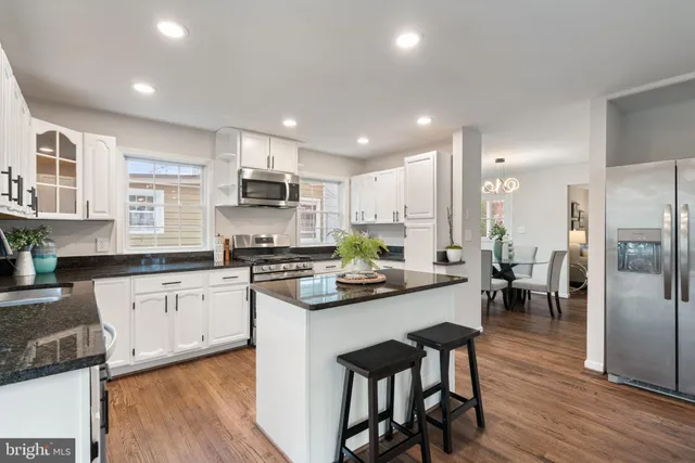 a kitchen with stainless steel appliances granite countertop a refrigerator a stove top oven a sink and white cabinets with wooden floor