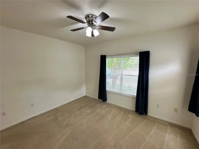 an empty room with chandelier fan and windows