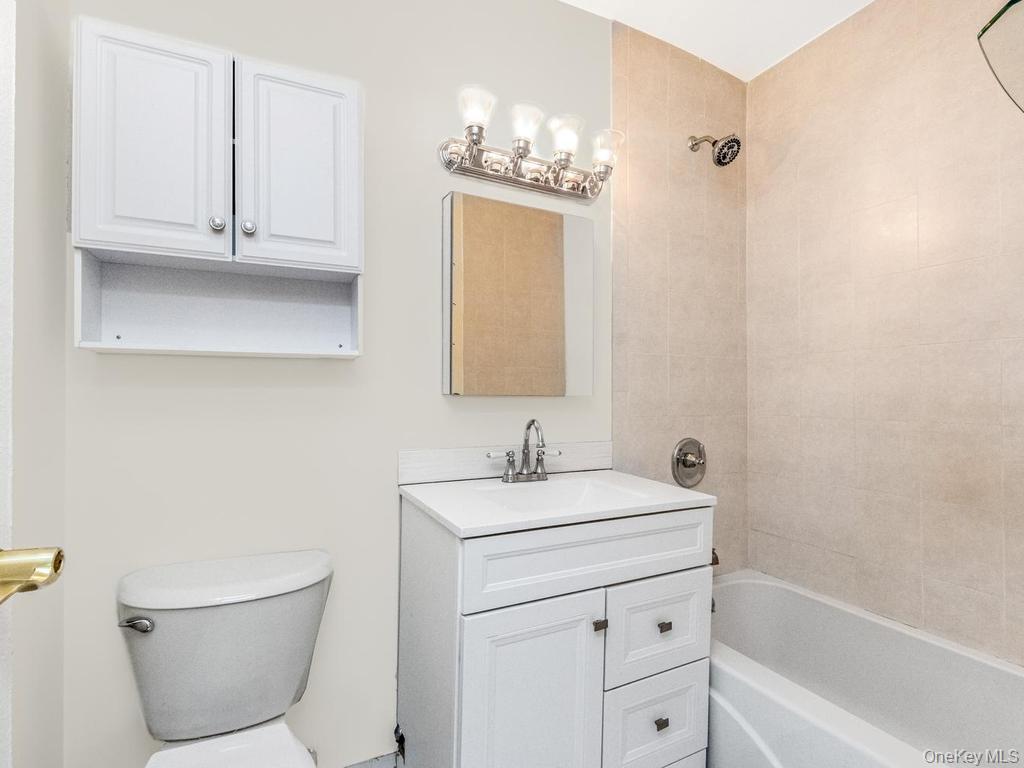 25 Trinity Place, Unit 3J New Rochelle, NY 10805 - Photo 5 of 15 Bathroom featuring a white vanity with integrated sink, white storage cabinet, ceramic tile shower surround, chrome fixtures, and a four-light vanity bar