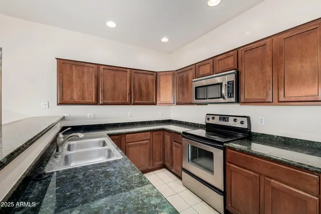 a kitchen with granite countertop a sink a stove top oven and wooden cabinetry