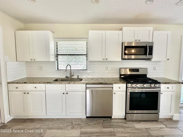 a kitchen with stainless steel appliances granite countertop grey cabinets a stove a sink and a microwave