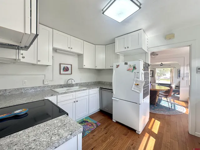 a kitchen with a refrigerator a stove a sink and white cabinets with wooden floor