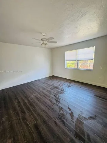 an empty room with wooden floor chandelier fan and windows