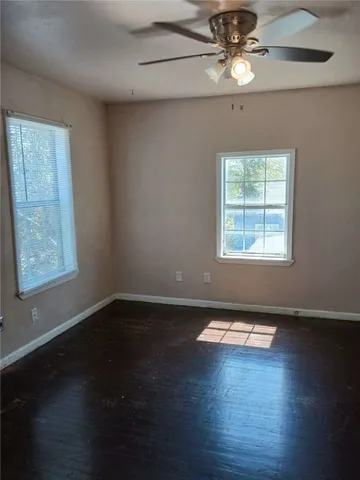 an empty room with wooden floor chandelier fan and windows