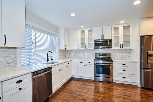 a kitchen with stainless steel appliances white cabinets a sink a stove a refrigerator and microwave