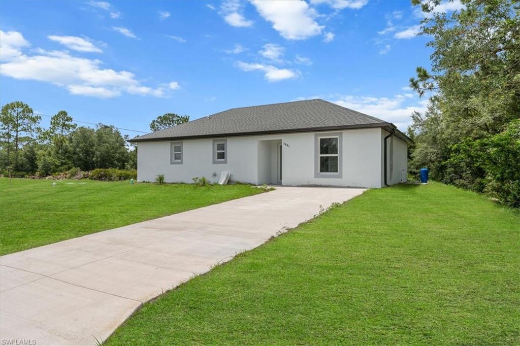 View of front of house with stucco siding, a front yard, concrete driveway, and a shingled roof