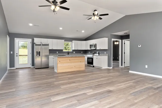 a view of kitchen with stainless steel appliances kitchen island a stove a refrigerator cabinets and living room view