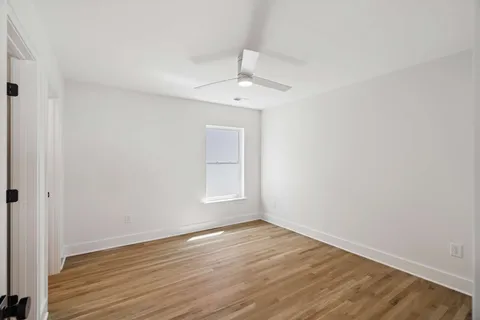 an empty room with wooden floor ceiling fan and window